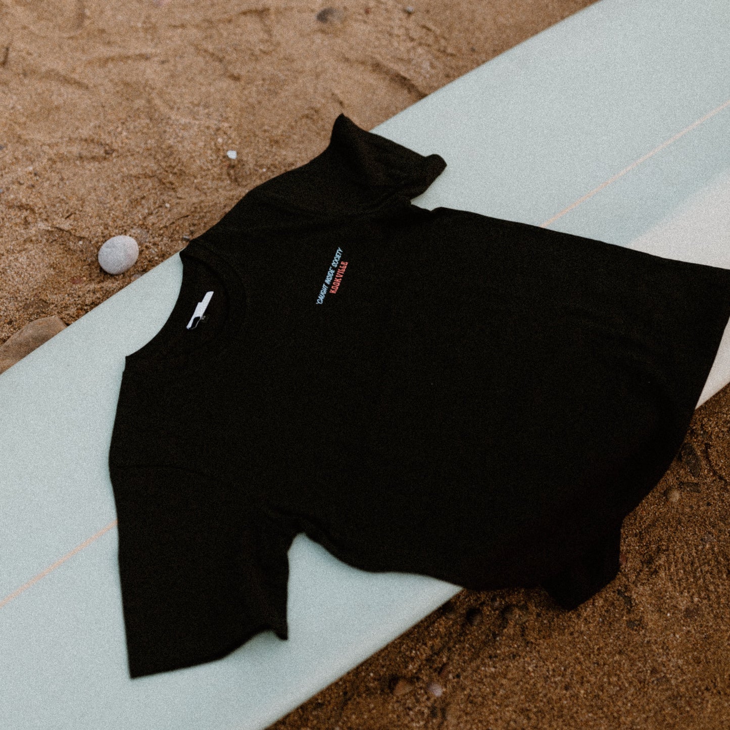 Black t shirt on a surfboard on a sandy beach