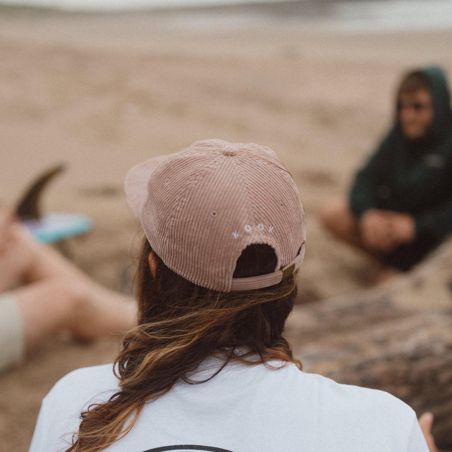Person wearing a white t-shirt with 'Kookville Surf Co' on the beach