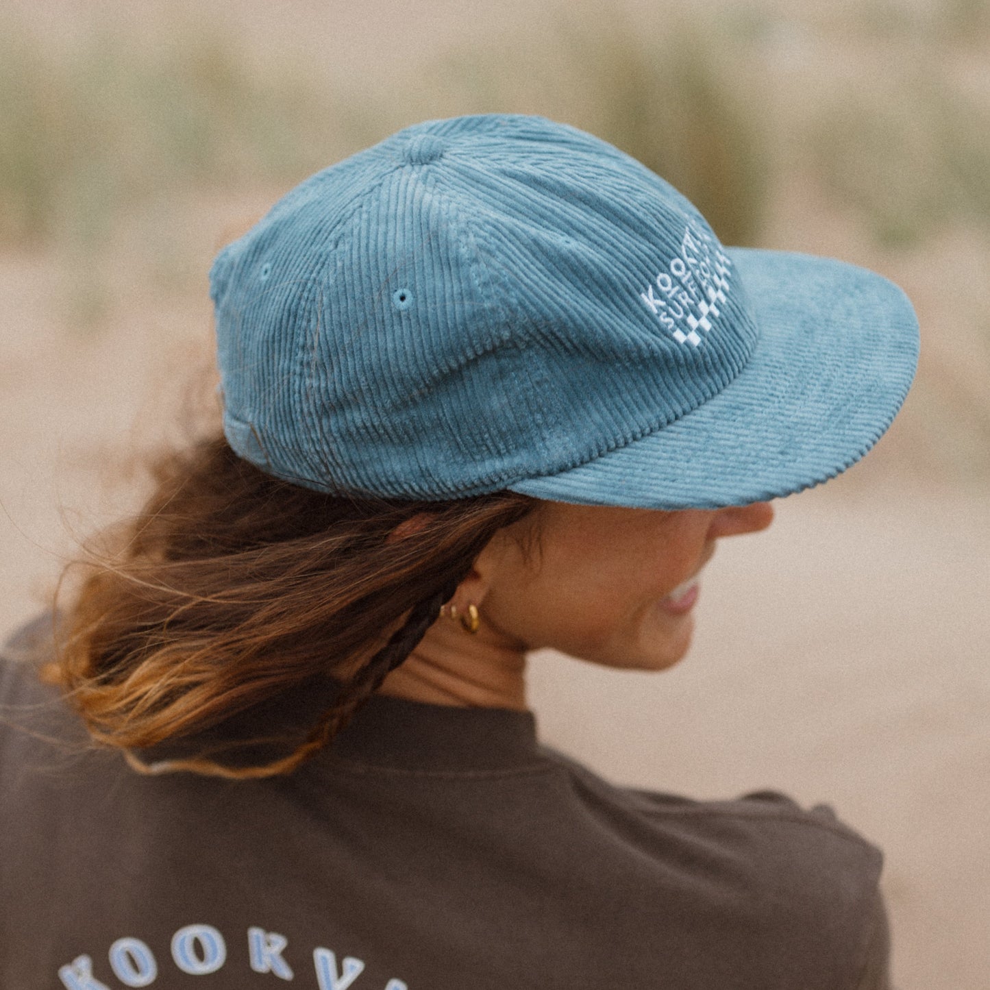 Person wearing a blue cap and brown t-shirt with 'Kookville Surfwear' logo.