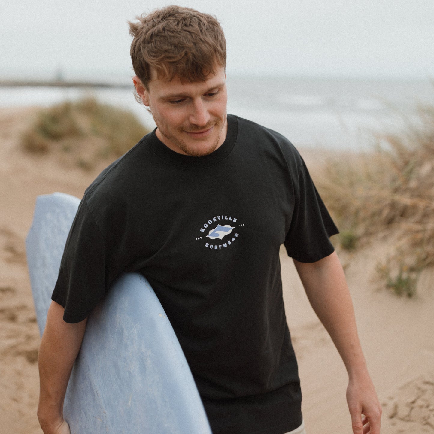 Man holding a surfboard on a beach with a neutral background