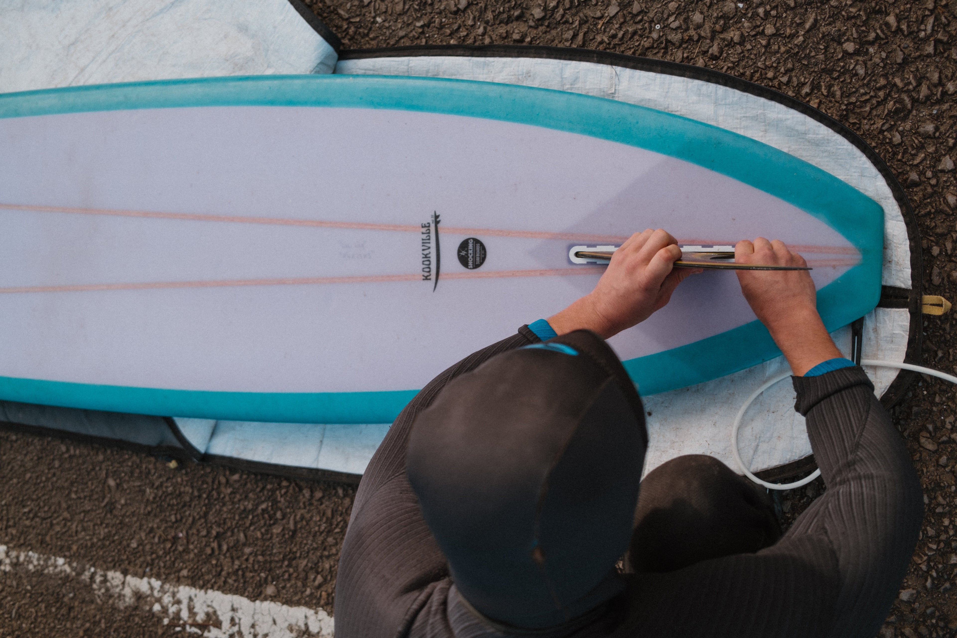 Person adjusting a surfboard with a visible brand logo on a textured surface