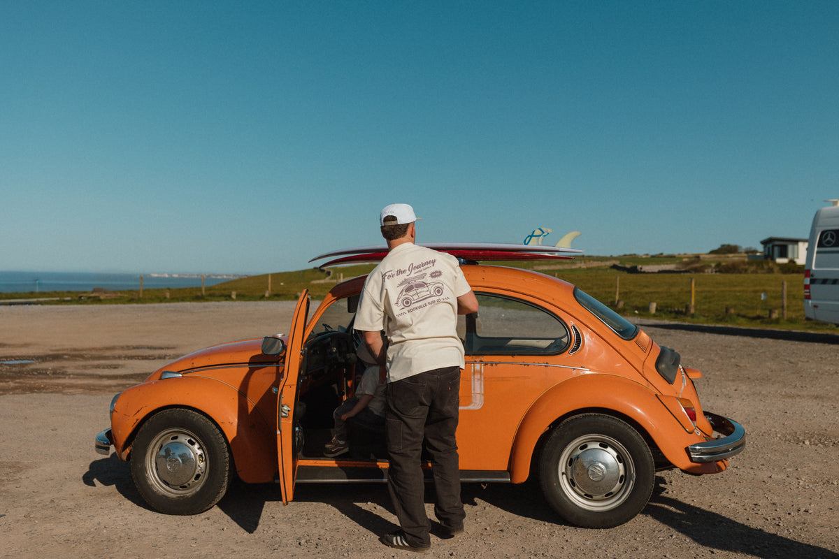 Man getting into an orange vintage car with a clear blue sky and ocean view.