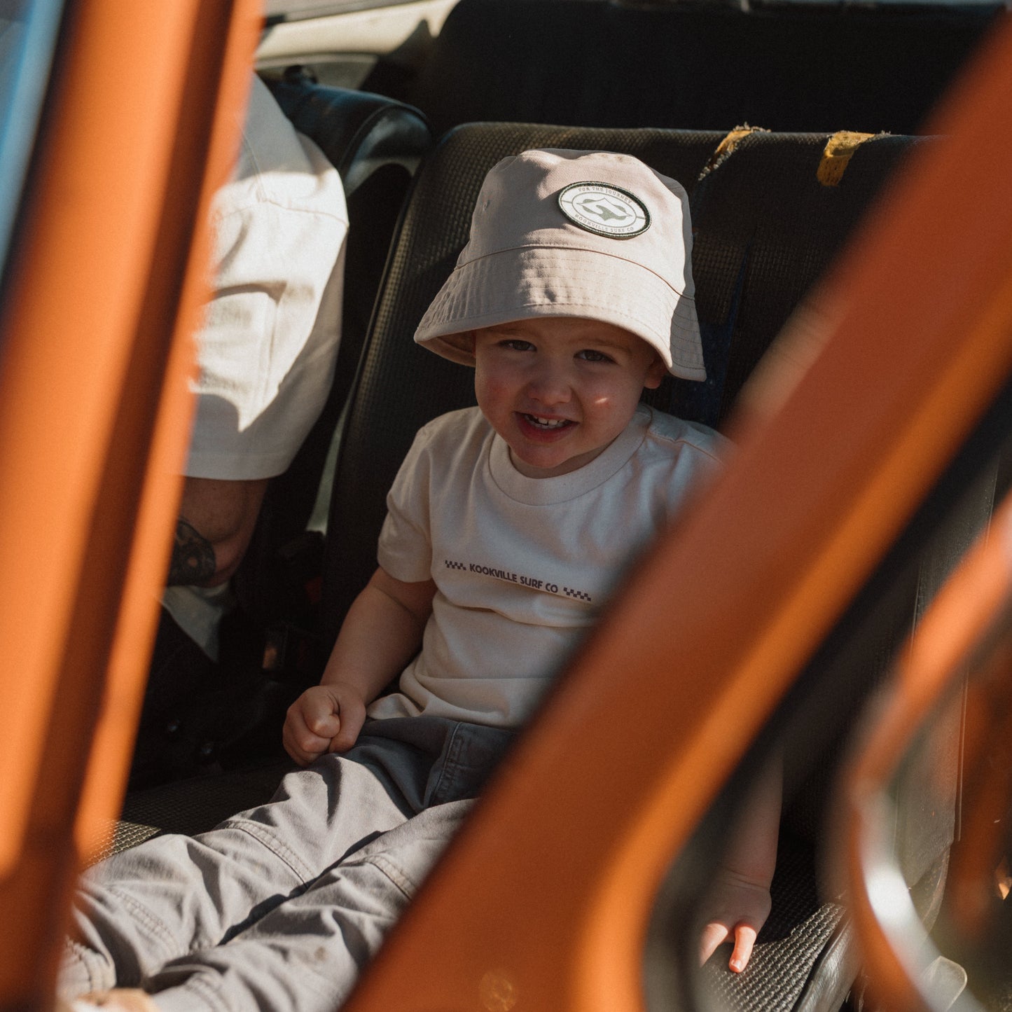 Child sitting in a car seat with a hat, looking out of an open car door.
