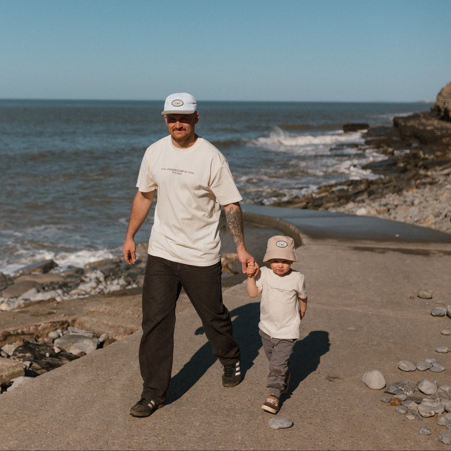 Man and child walking along a rocky beach with clear blue sky