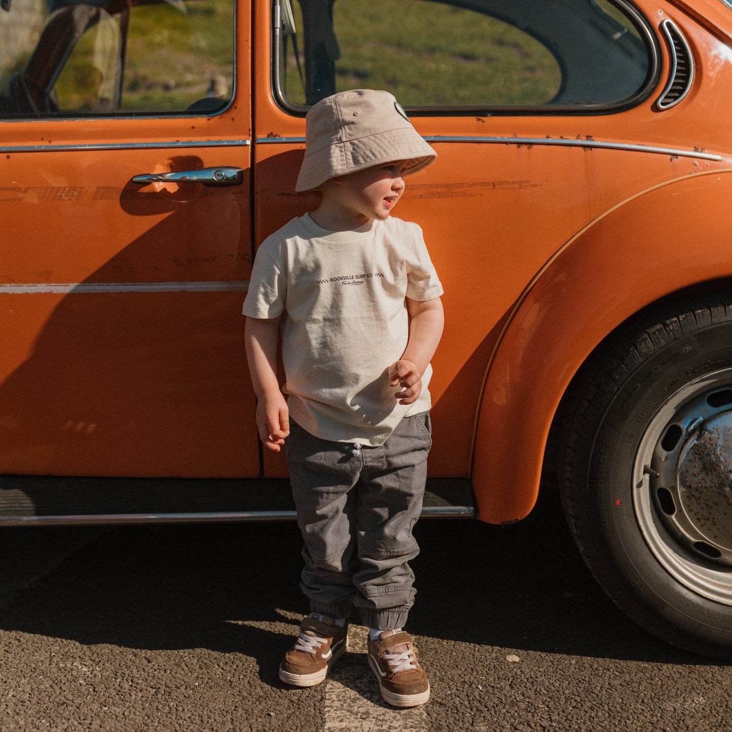 Child standing next to an orange vintage car on a sunny day