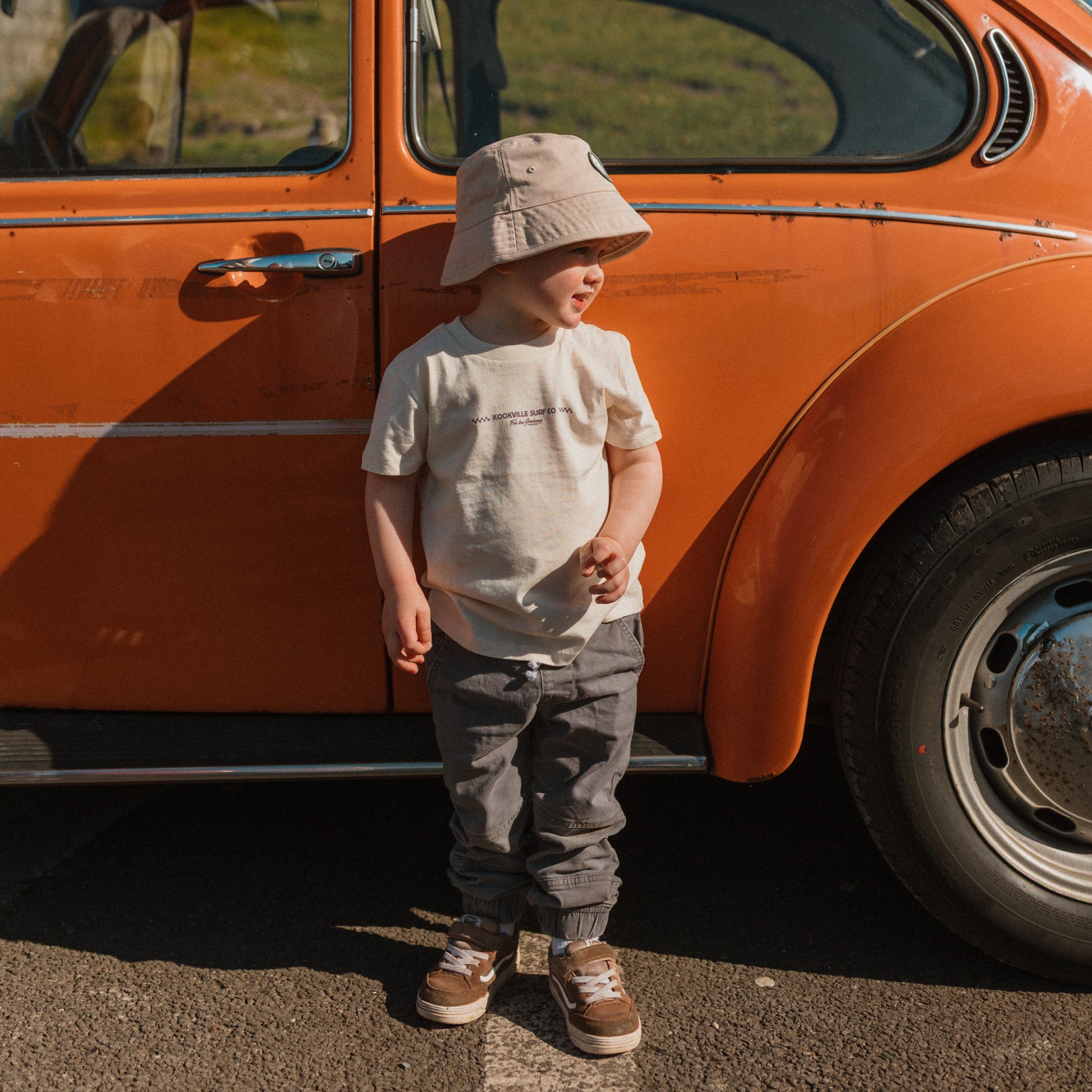 Child standing next to an orange vintage car on a sunny day