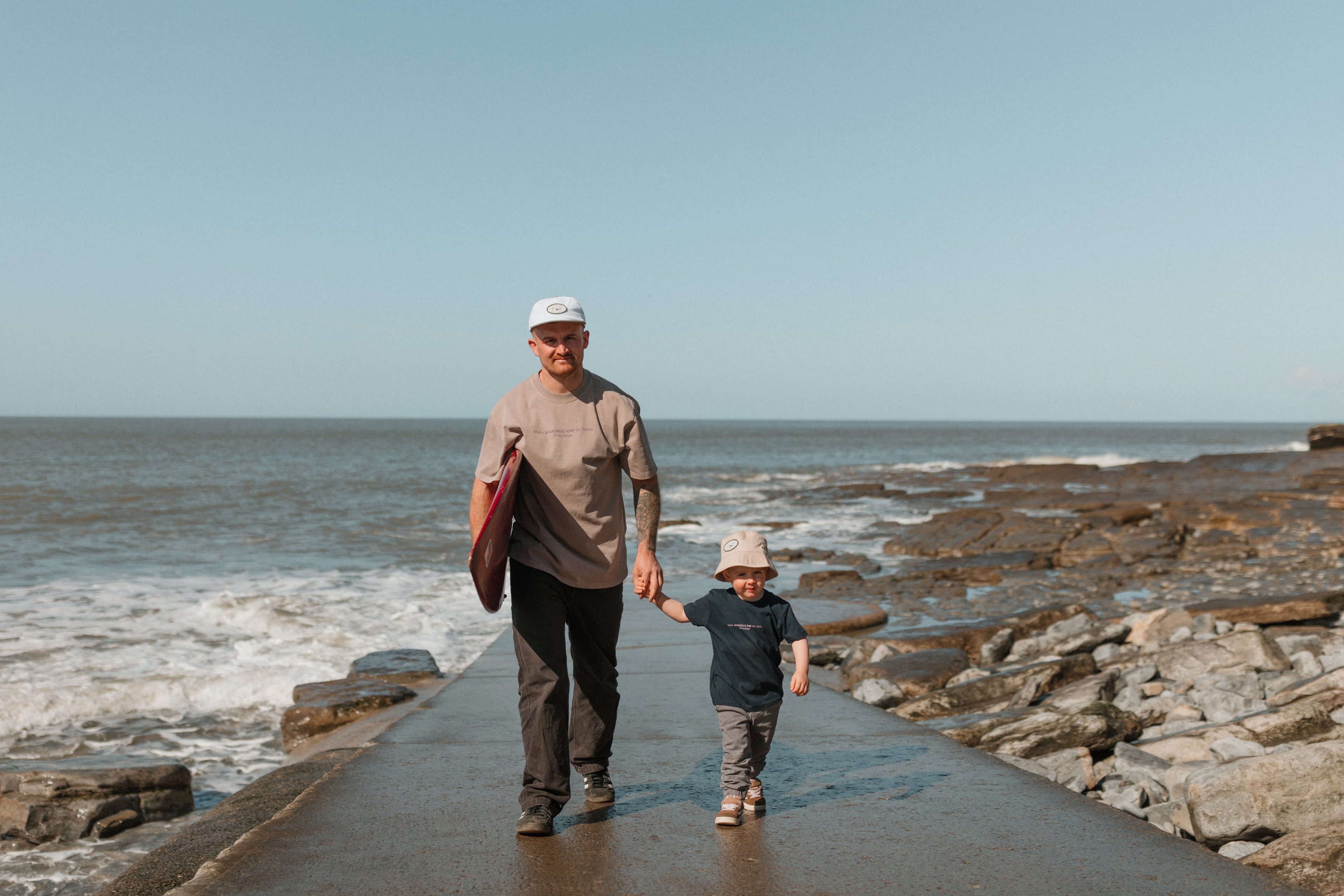 Man and child walking along a rocky beach path with ocean waves in the background.