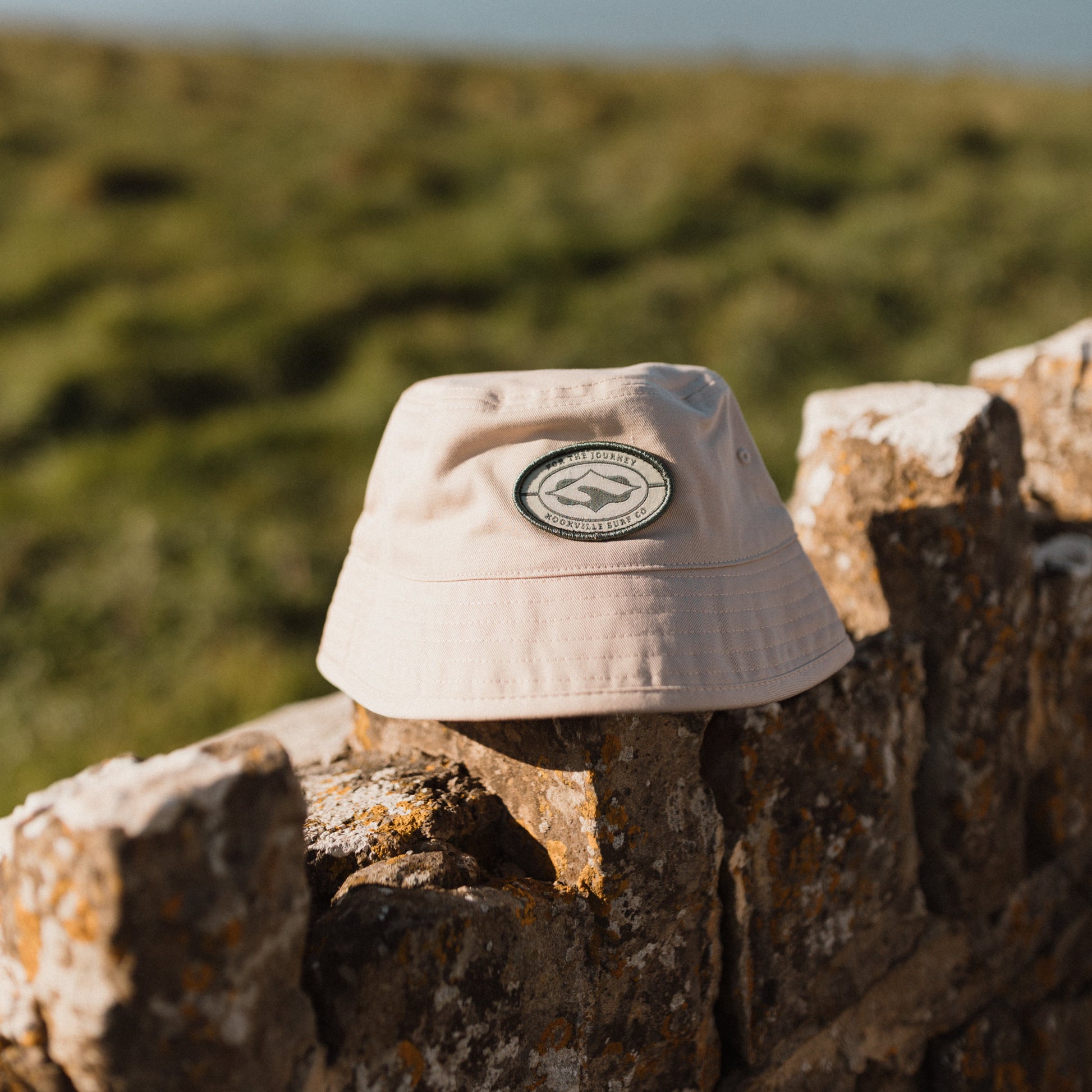 Pink bucket hat with a logo on a stone wall with a scenic background