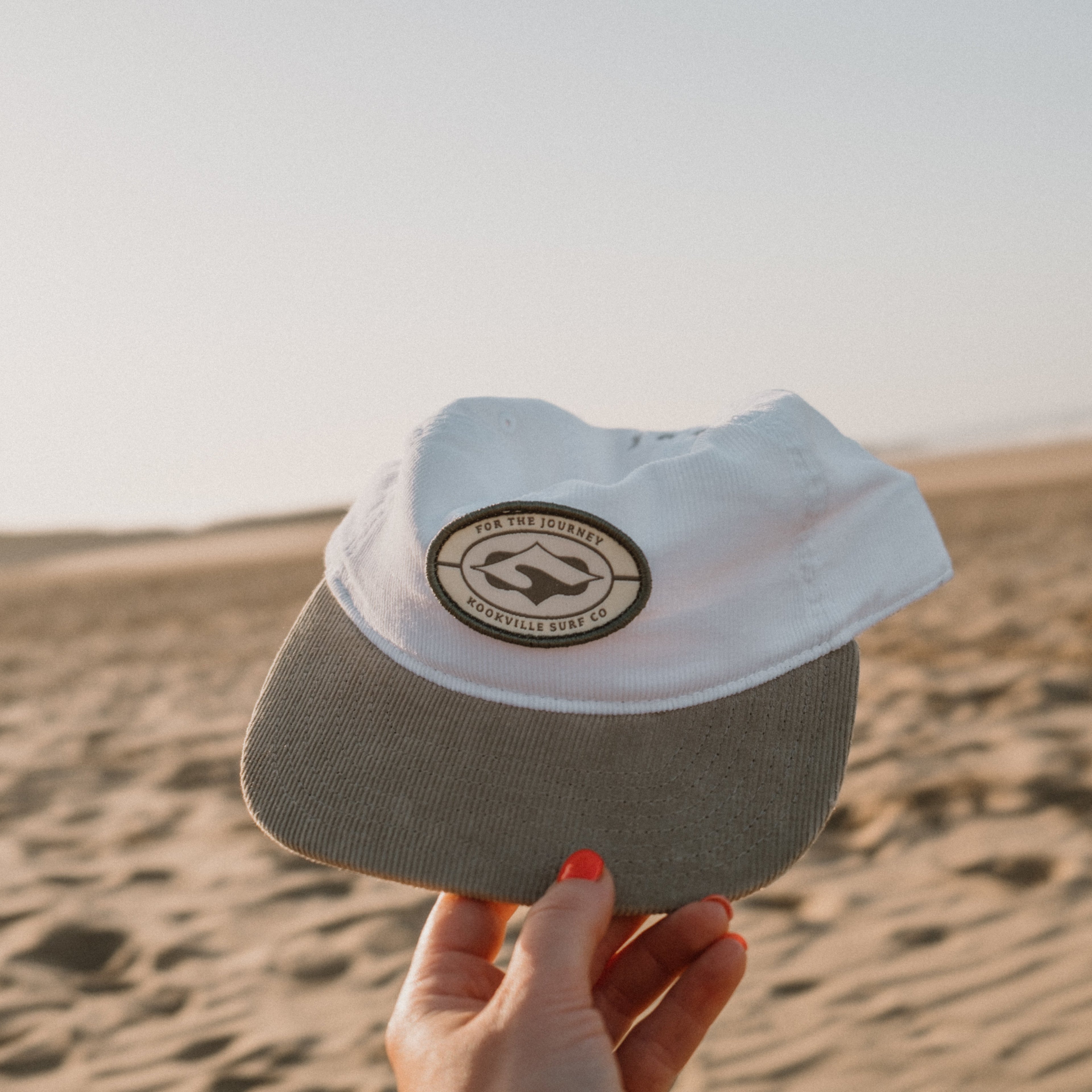 White cap with a logo held in front of a desert landscape