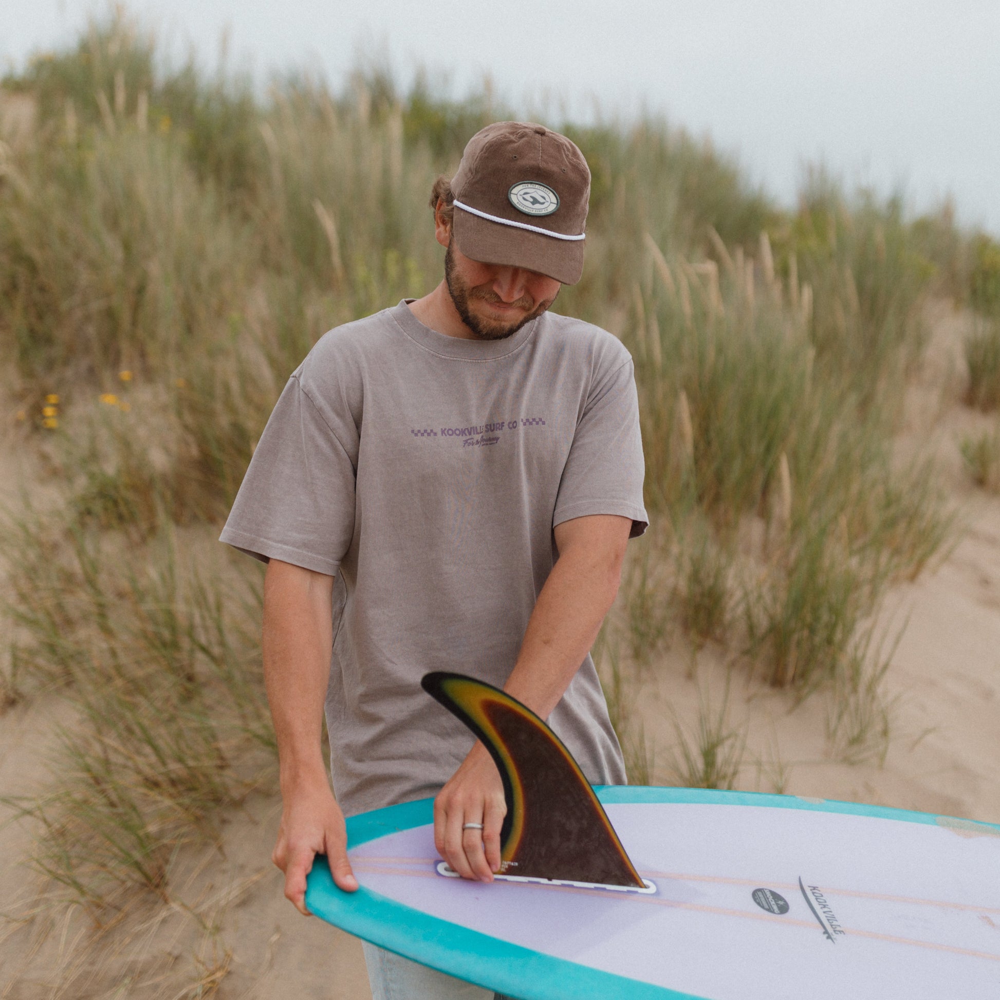 surfer holding a surfboard on a sandy beach wearing a hat