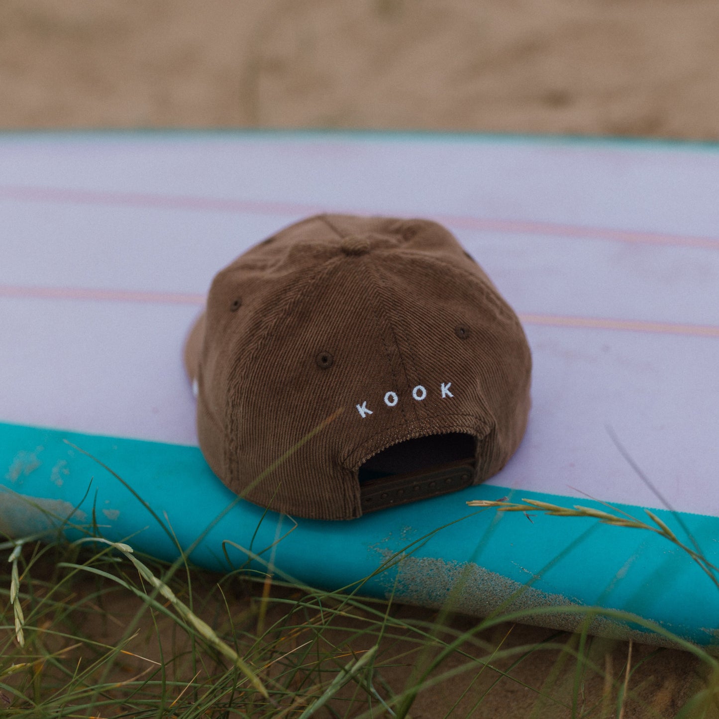 Brown cap with 'ROOK' logo on a surfboard on a sandy beach