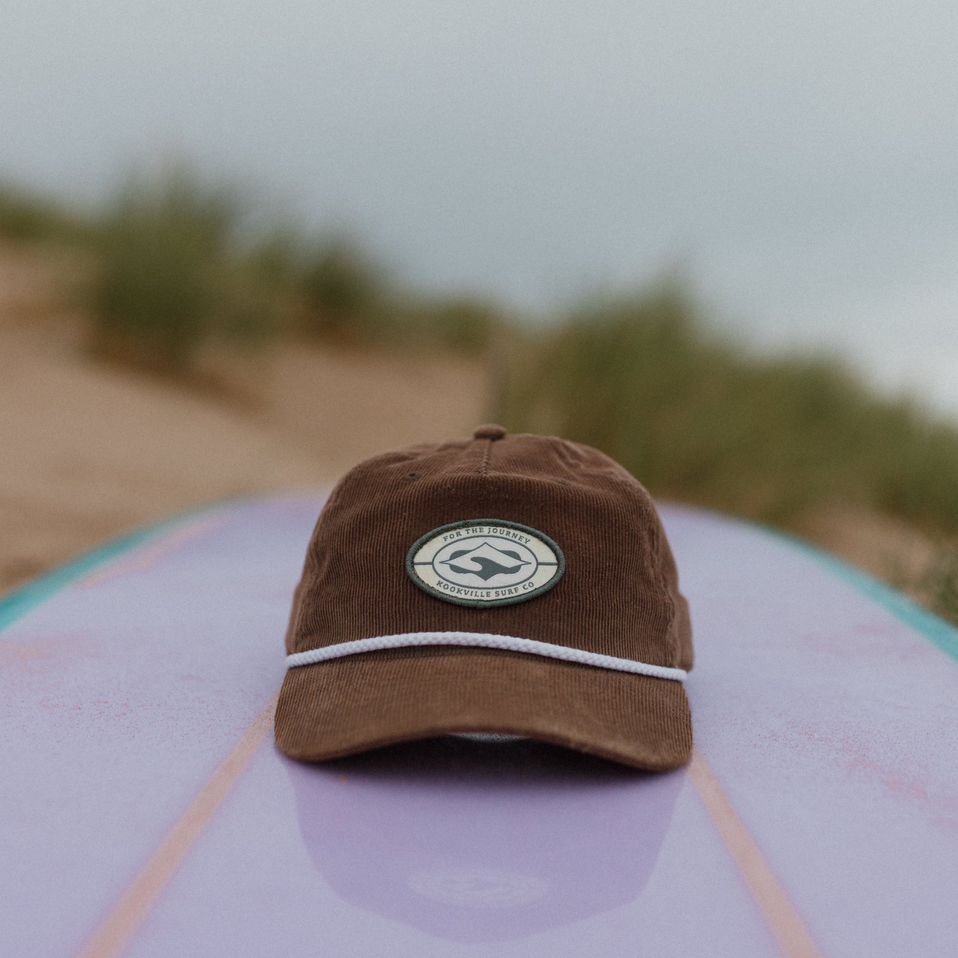 Brown cap with a logo on a surfboard on a beach