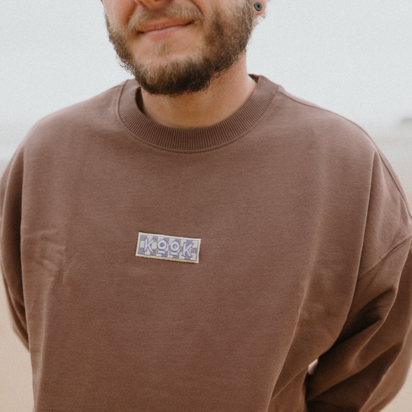 Man wearing a brown sweatshirt with a logo on a blurred background