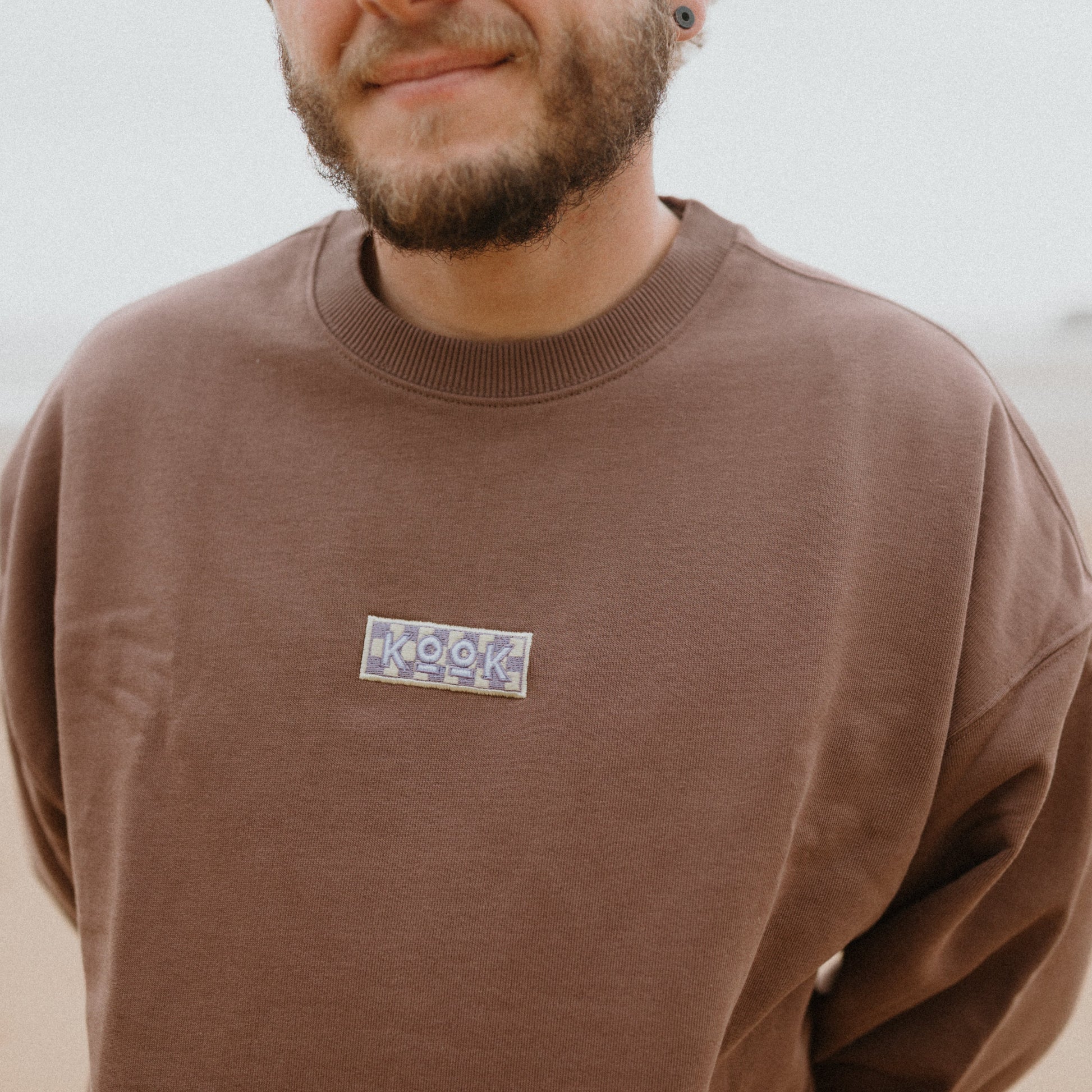 Man wearing a brown sweatshirt with a logo on a blurred background