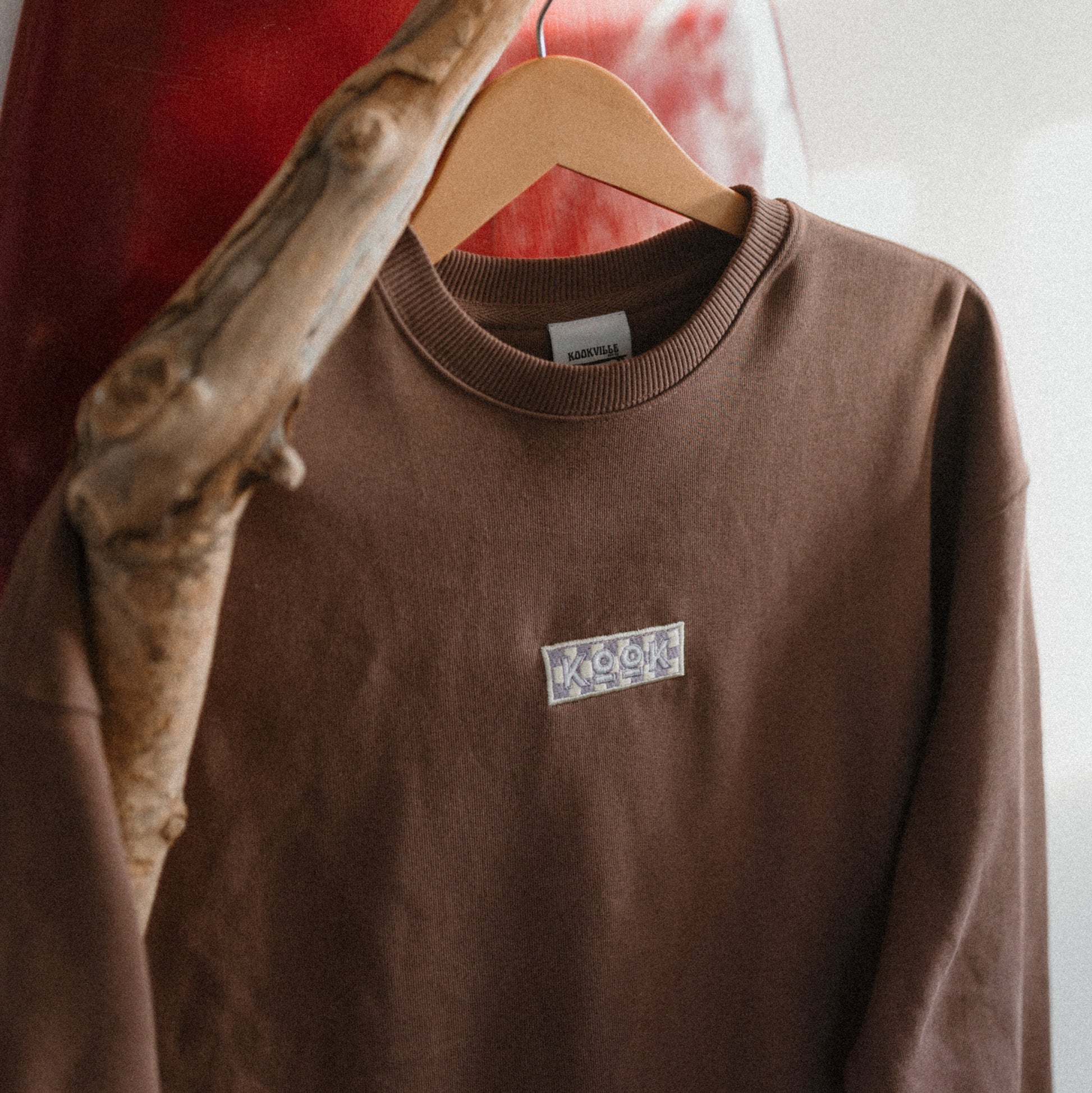 Brown sweatshirt with a logo on a hanger against a red and white abstract background