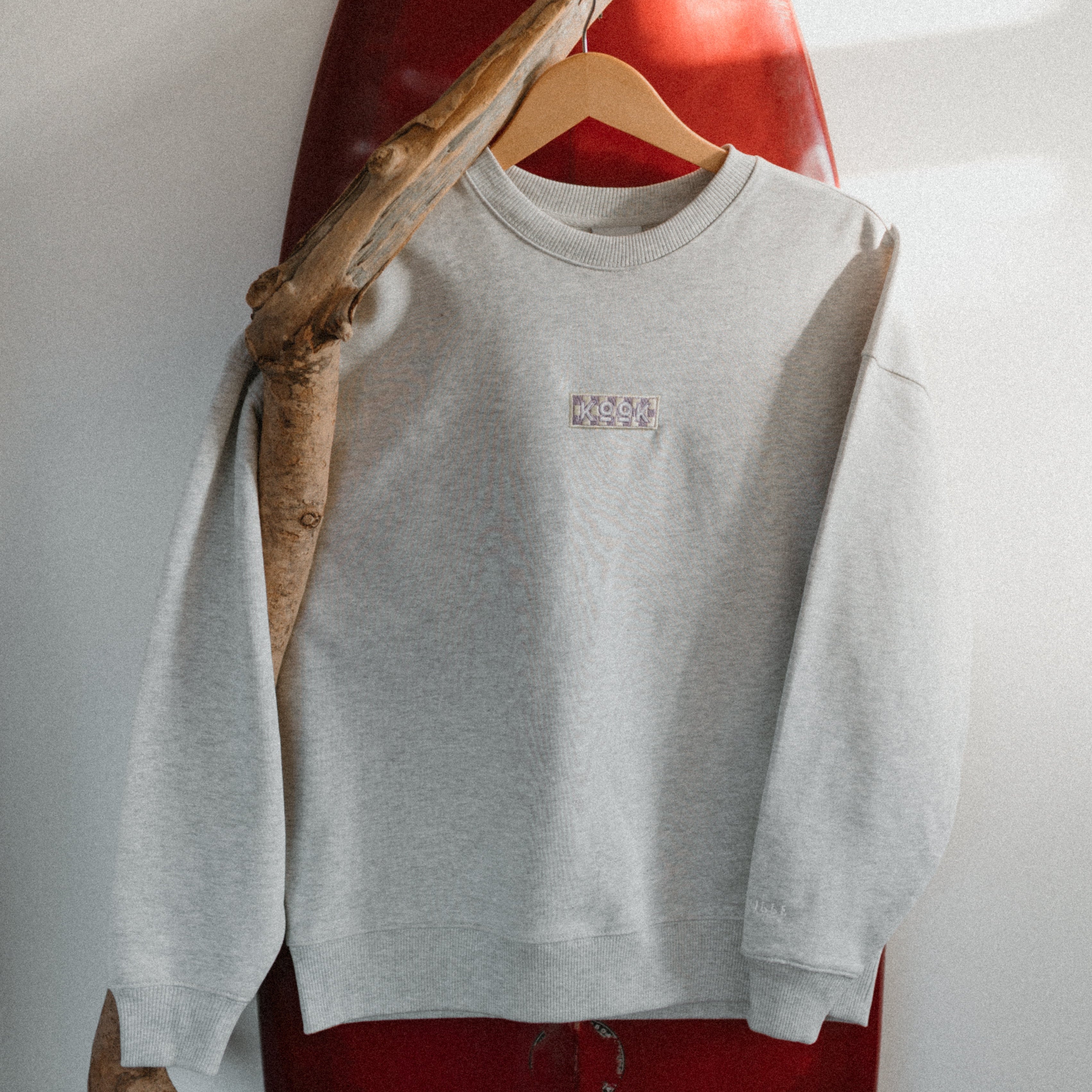 Gray sweatshirt with a logo on a hanger against a white wall.