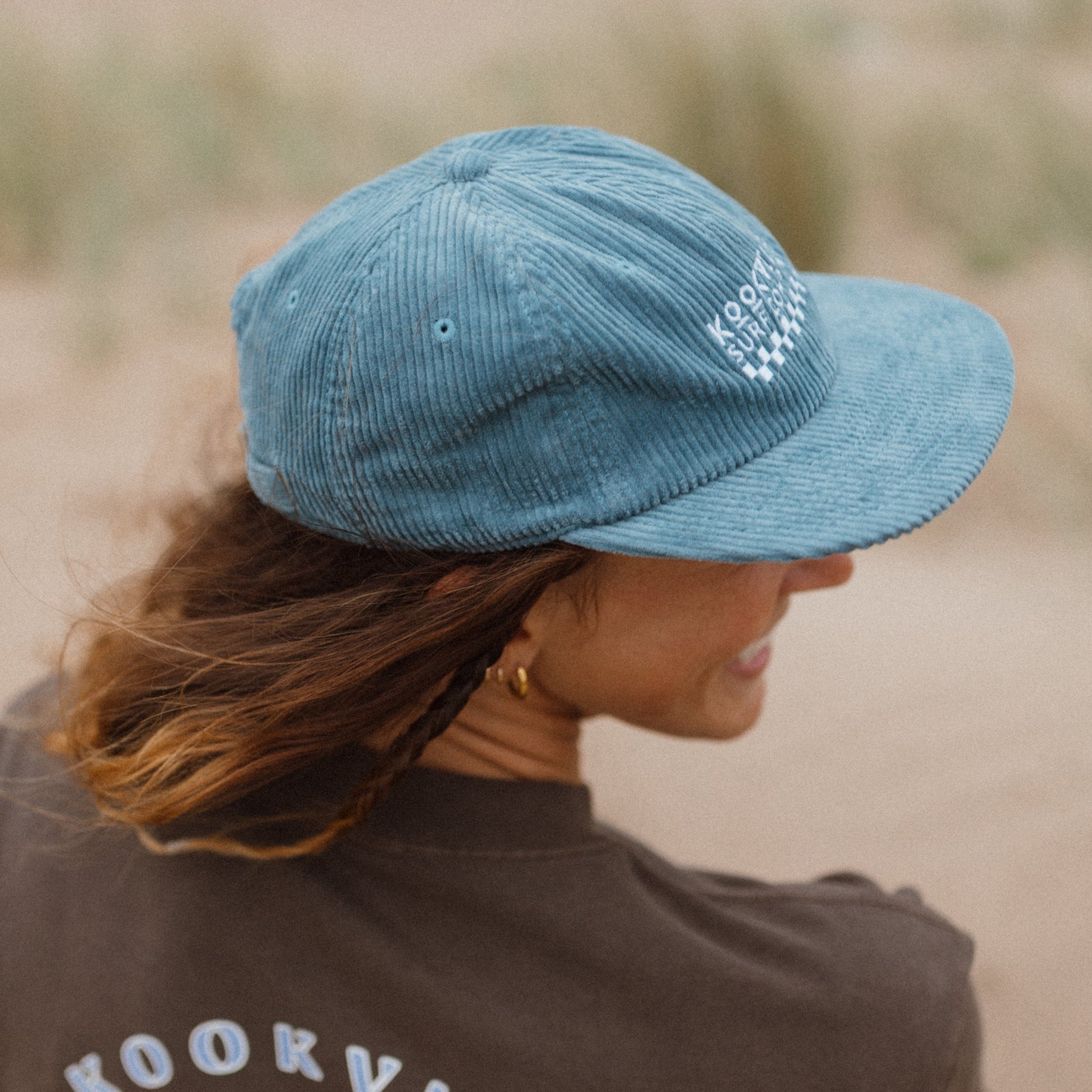 Person wearing a blue cap and brown t-shirt with 'Kookville Surfwear' logo.